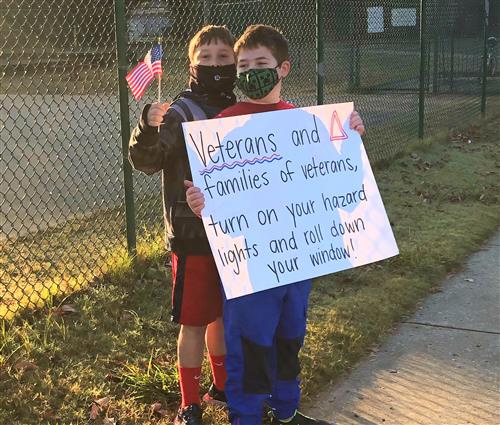 students with sign saying roll down windows and flash hazard lights if a veteran
